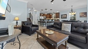 Un salon spacieux avec un canapé en cuir foncé, une table basse en bois et un coin repas agrémenté d’un lustre.