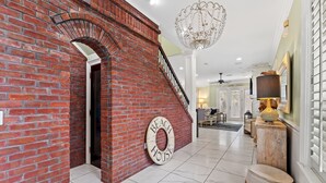 Un hall d’entrée spacieux avec un mur en briques, un lustre et une enseigne indiquant « MAISON DE PLAGE ».