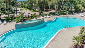 Une grande piscine à bords incurvés, entourée de palmiers et de chaises longues.