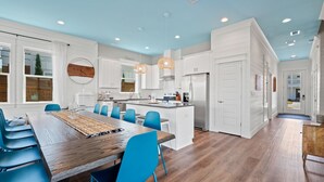 Una cucina moderna con mobili bianchi, un tavolo da pranzo in legno con sedie blu e un'isola centrale con un frigorifero.