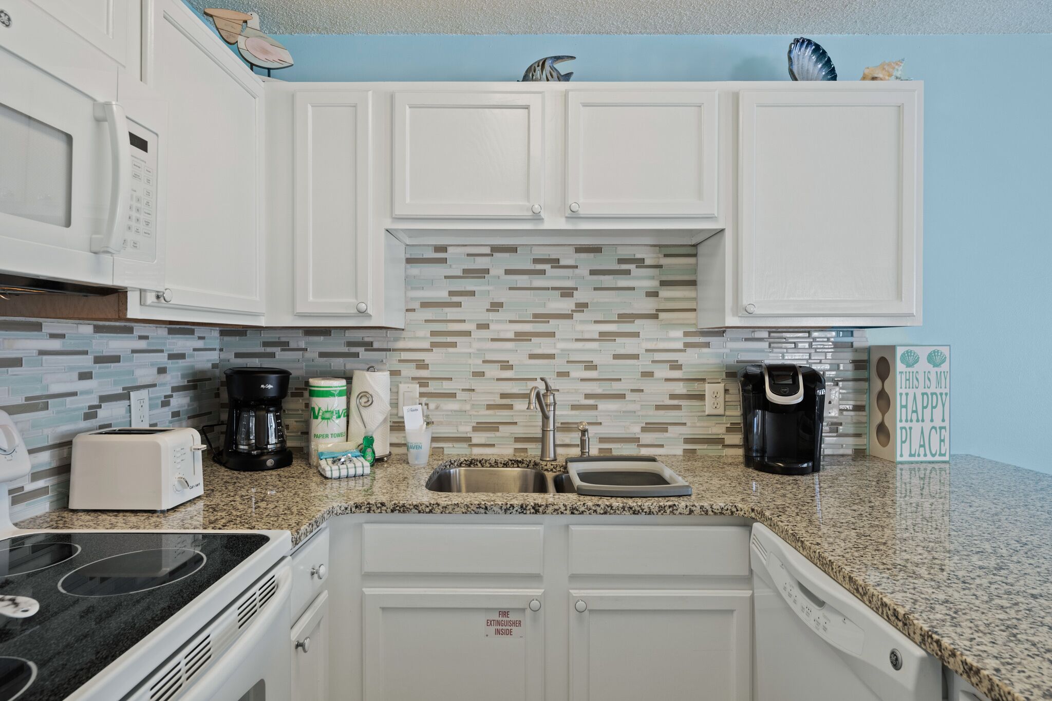 A kitchen with white cabinets, a granite countertop, a toaster, a coffee maker, and a dishwasher.