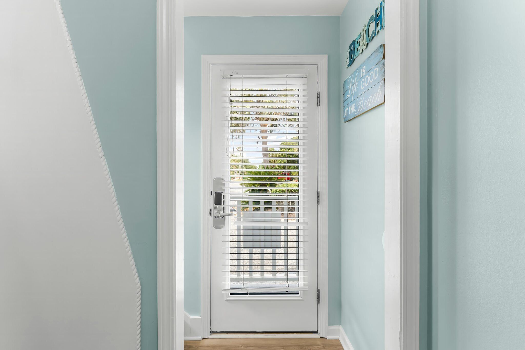 A white door with a metal grill and a white handle, set in a hallway with light blue walls and a wooden floor.