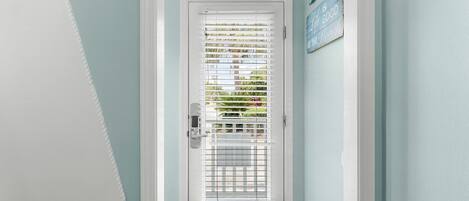 A white door with a metal grill and a white handle, set in a hallway with light blue walls and a wooden floor.