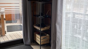 Een kamer met een televisie op een standaard, een houten vloer, een betegelde deuropening en uitzicht door een raam met gordijnen.