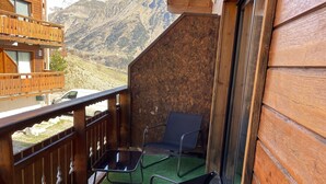 Een houten balkon met twee zwarte stoelen en een kleine tafel, met uitzicht op een bergachtig landschap.