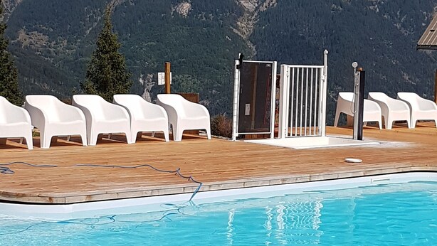 Zwembadgedeelte met houten terras, witte lounge stoelen en een uitzicht op bergen op de achtergrond.