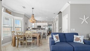 Une cuisine moderne avec des meubles blancs, un lustre et un coin repas comprenant des chaises et une table en bois.