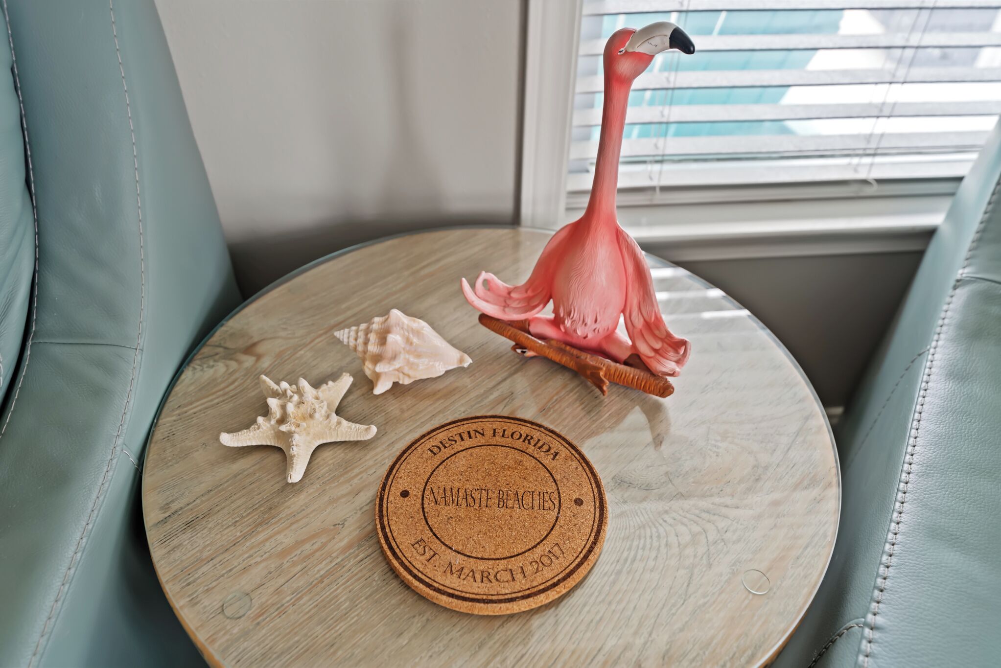 A wooden table with a coaster, a flamingo figurine, and seashells.