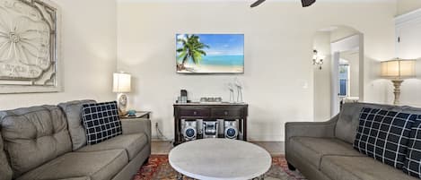 Un soggiorno con due divani, un tavolino da caffè, una televisione, una ventola a soffitto e un elemento decorativo a parete.