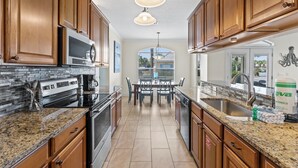 A kitchen with granite countertops, stainless steel appliances, wooden cabinets, and a dining area with a table and chairs. - Gated Community ~ Spacious Living ~ Patio (Miramar Beach)