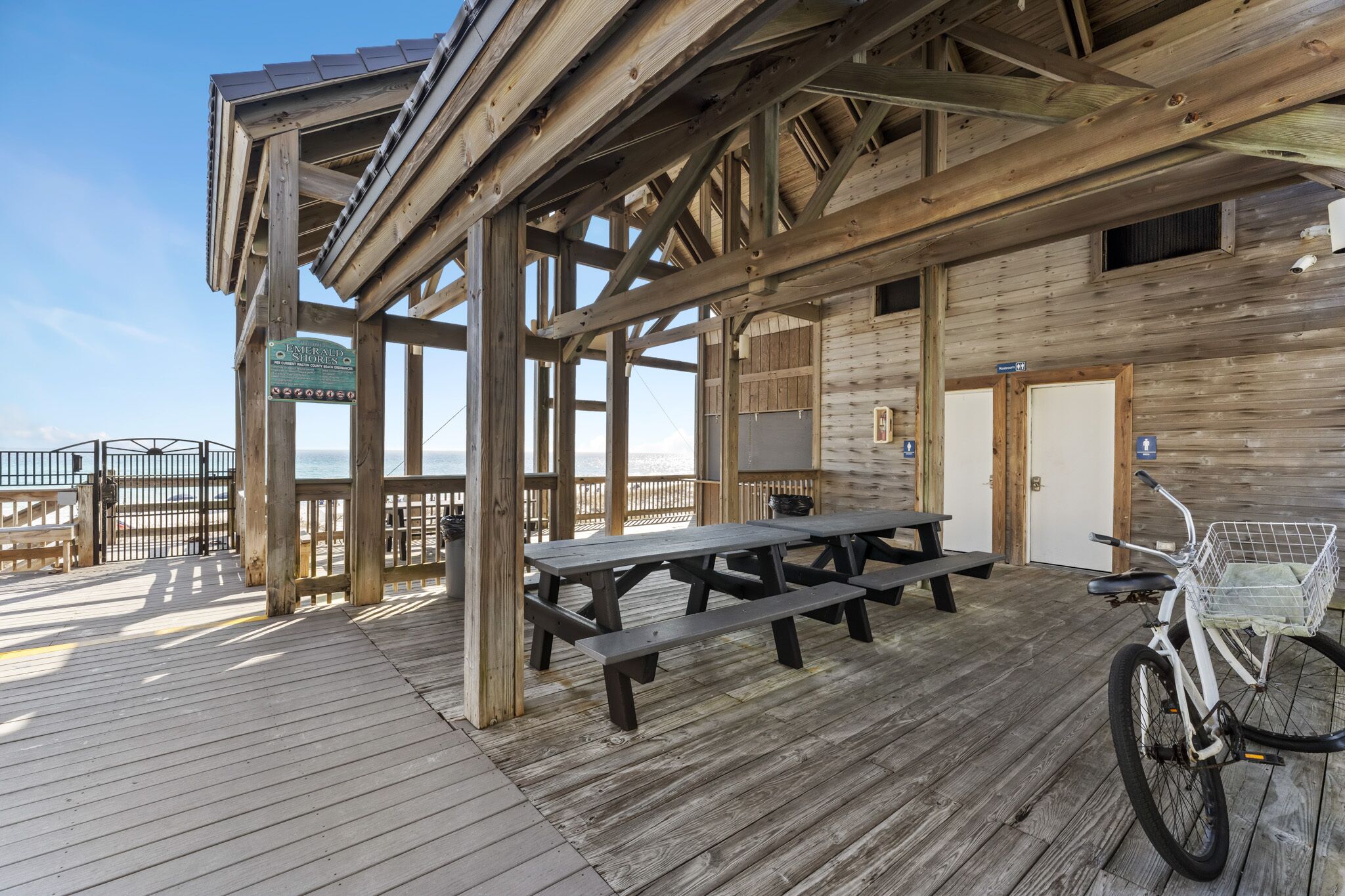 A wooden deck with picnic tables and a bicycle, overlooking a beach.