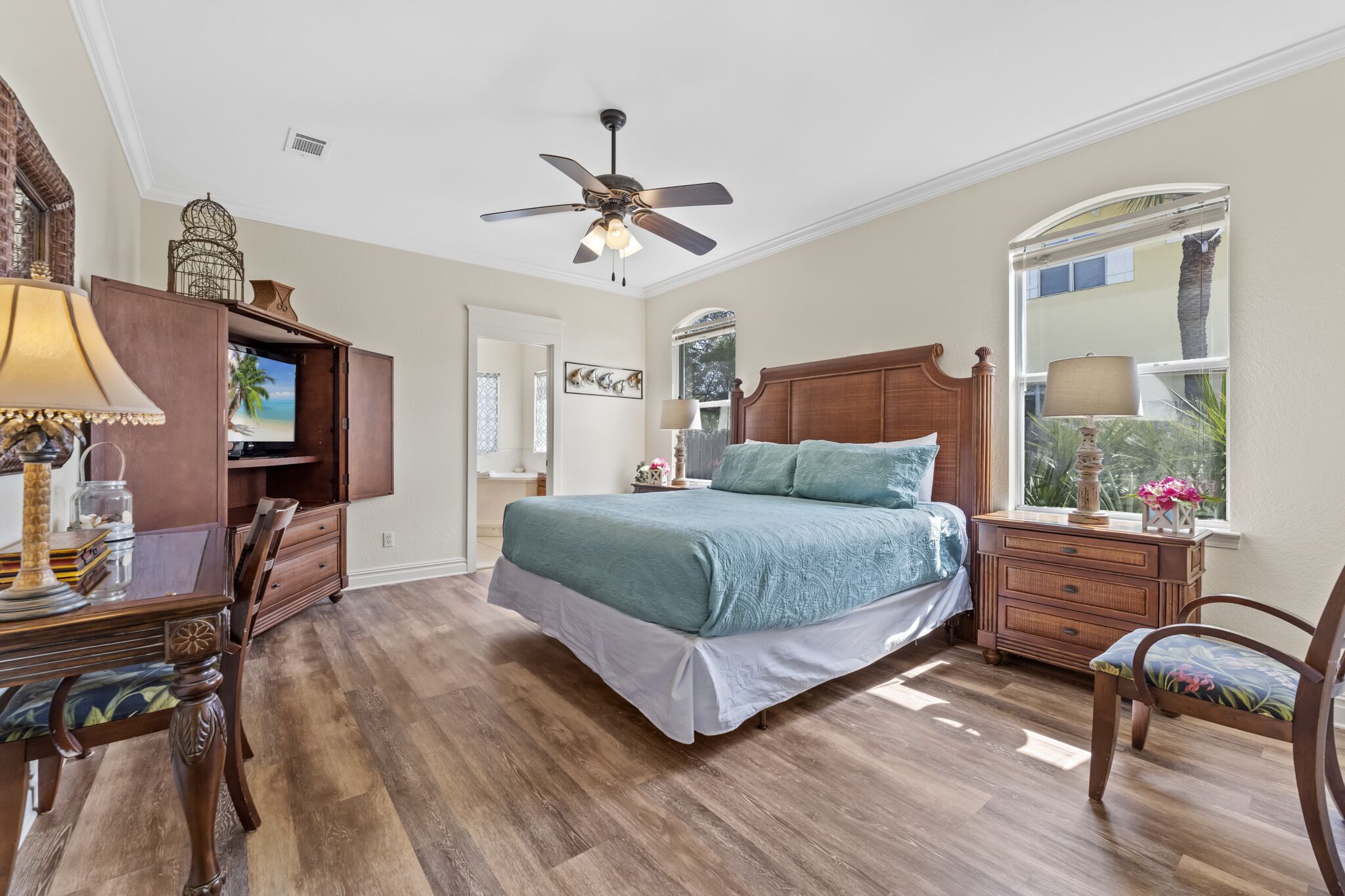 A bedroom with a bed, wooden furniture, a ceiling fan, a window with a view, and a TV on a cabinet.