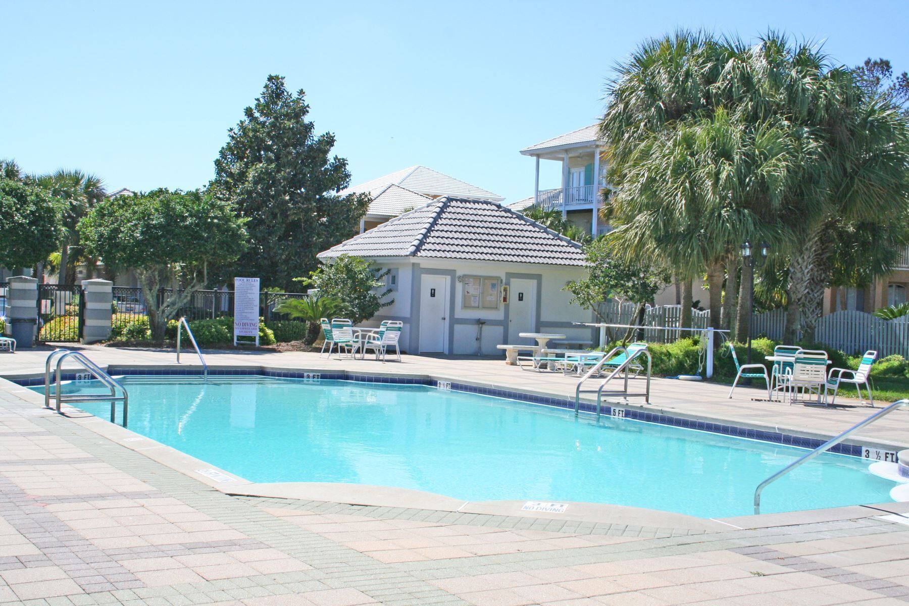 A swimming pool with a tiled deck, lounge chairs, and a small building with a tiled roof.