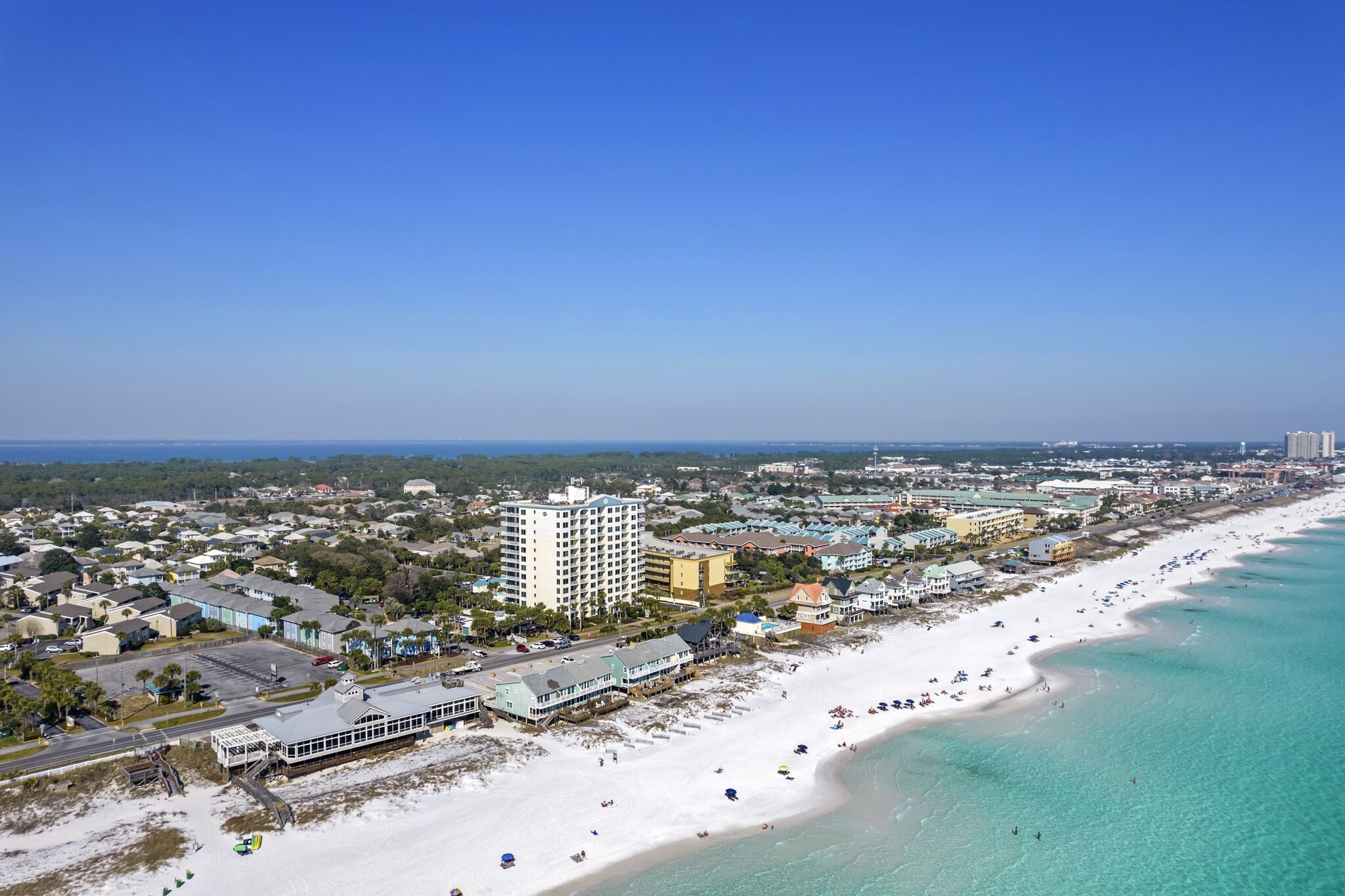 Un paisaje urbano costero con una playa extensa, hoteles frente al mar y un cielo azul despejado.