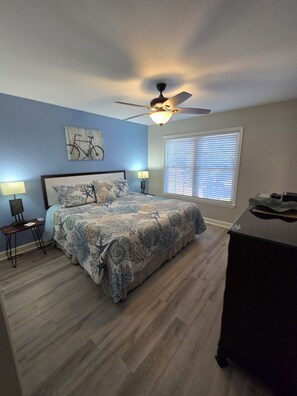 A bedroom with a bed, a ceiling fan, a window with blinds, and a desk.