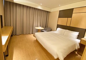 A hotel room with a large bed, a desk, a chair, and a small table. - Ji Hotel (Nanjing)