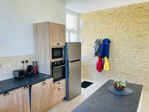A modern kitchen with wooden cabinets, a built-in oven, a refrigerator, and a stone wall.