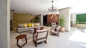 Ein modernes Wohnzimmer mit einer Couch, Sesseln und einem Couchtisch. Pflanzen und eine Wand aus Holz verleihen dem Raum Akzente.
