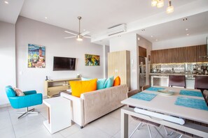 A modern living room with a sofa, a dining table, and a kitchen area with wooden cabinets and a built-in oven.