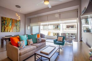 A modern living room with a sofa, coffee table, and armchair, large windows, and a balcony with outdoor furniture.