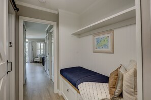 Un pasillo estrecho que conduce a un dormitorio con una cama, un mapa en la pared y una silla al fondo.