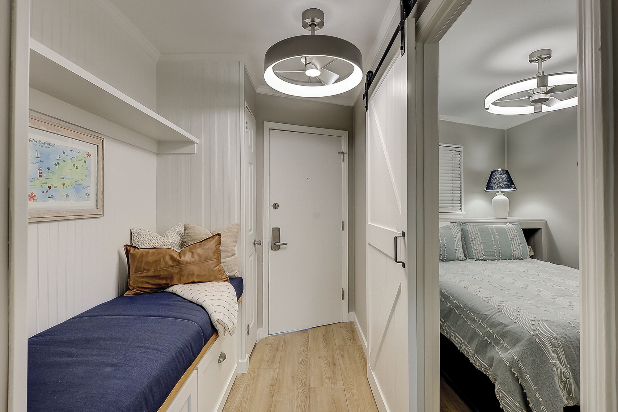 A narrow hallway leading to a bedroom with a bed, a nightstand, and a lamp.