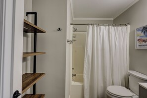 Un baño con cortina de ducha, inodoro y repisas.