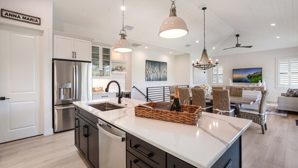 A modern kitchen with a large island, stainless steel appliances, and a dining area with wicker furniture and a TV.