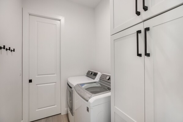 A laundry room with a front-loading washer and dryer, white cabinets, and black handles. - Private Pool! Ping-Pong, Pool Table, Putt-Putt! (Holmes Beach)
