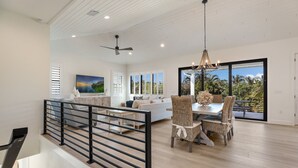 A spacious living area with a dining set, a ceiling fan, and a large window offering a view of palm trees.