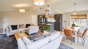 A modern living room with a sofa set, a dining table with chairs, and a kitchen area with a bar. - Host & Stay | Eller Beck - The Cabin in the Woods (Whitby)