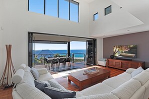 A modern living room with a large sofa, a coffee table, and a TV. There is a balcony with a view of the ocean. - Luxury, magnificent views, space and swimming pool (Point Lookout)