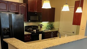 Cucina con mobili in legno scuro, frigorifero nero, piano di lavoro in granito e illuminazione a sospensione.