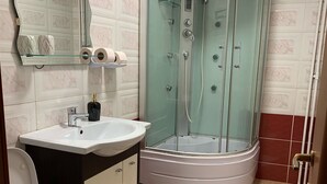 Moderni kylpyhuone, jossa on lasiseinällä varustettu suihku, valkoinen pesuallas ja wc.