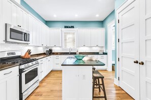A modern kitchen with white cabinets, a stainless steel microwave, a stove, and a glass island with stools.