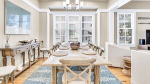 A dining area with a large wooden table, white upholstered chairs, and a chandelier. - Gorgeous Watercolor Home Close to  Camp with NEW 6  "LSV" Low Speed Vehicle. (SANTA ROSA BEACH)