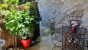 A patio area with a metal table and chairs, a red potted plant, and a wall with a textured surface. - House (Rochefort-du-Gard)