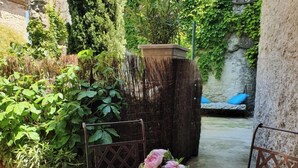A round metal table with a vase of pink flowers, surrounded by metal chairs, in a garden with a stone wall and greenery. - House (Rochefort-du-Gard)