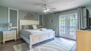 Un dormitorio con cama, mesitas de noche, cómoda, ventilador de techo y vista a través de una puerta de cristal.