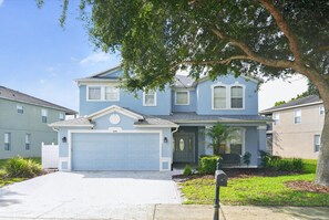 A bright front view of the home with a spacious driveway and lawn. - Disney-Themed Villa with Heated Pool & Playroom (Davenport)