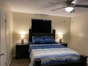 Une chambre à coucher comprenant un lit, deux tables de chevet, un ventilateur de plafond et une petite table de nuit avec une lampe.