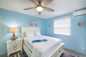 A bedroom with a bed, a nightstand, a lamp, a ceiling fan, and a window with blinds.