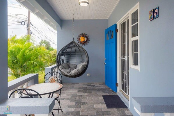 A balcony with a hanging chair, a table, and a blue door.