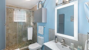 A modern bathroom with a glass shower enclosure, a toilet, a sink with a mirror, and a towel rack.