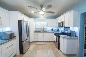 A modern kitchen with white cabinets, stainless steel appliances, granite countertops, and a ceiling fan.