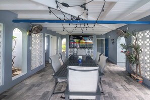 A covered outdoor dining area with a table and chairs, a TV screen displaying a menu, and a potted plant.