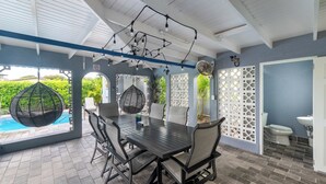 An outdoor patio with a table and chairs, a hanging chair, and a pool.