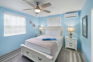 Une chambre à coucher comprenant un lit, deux tables de chevet, un ventilateur de plafond et un appareil de climatisation.