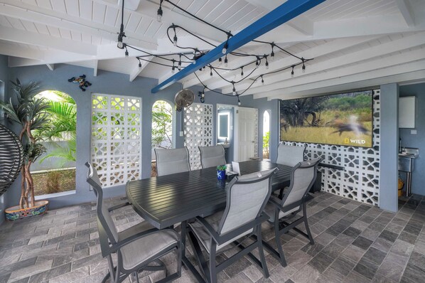 A conference room with a long table, chairs, a ceiling fan, and a large screen displaying a wildlife scene.