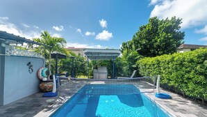 A swimming pool with a netted entry, surrounded by a tiled deck and lush greenery.